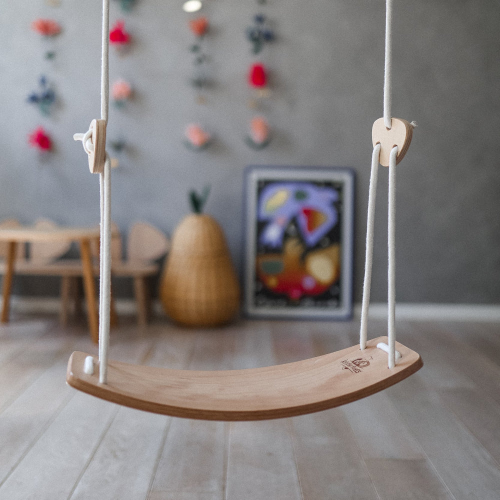 Kinderfeets child's swing hanging from a sturdy frame, featuring a wooden seat and safety straps for young children.