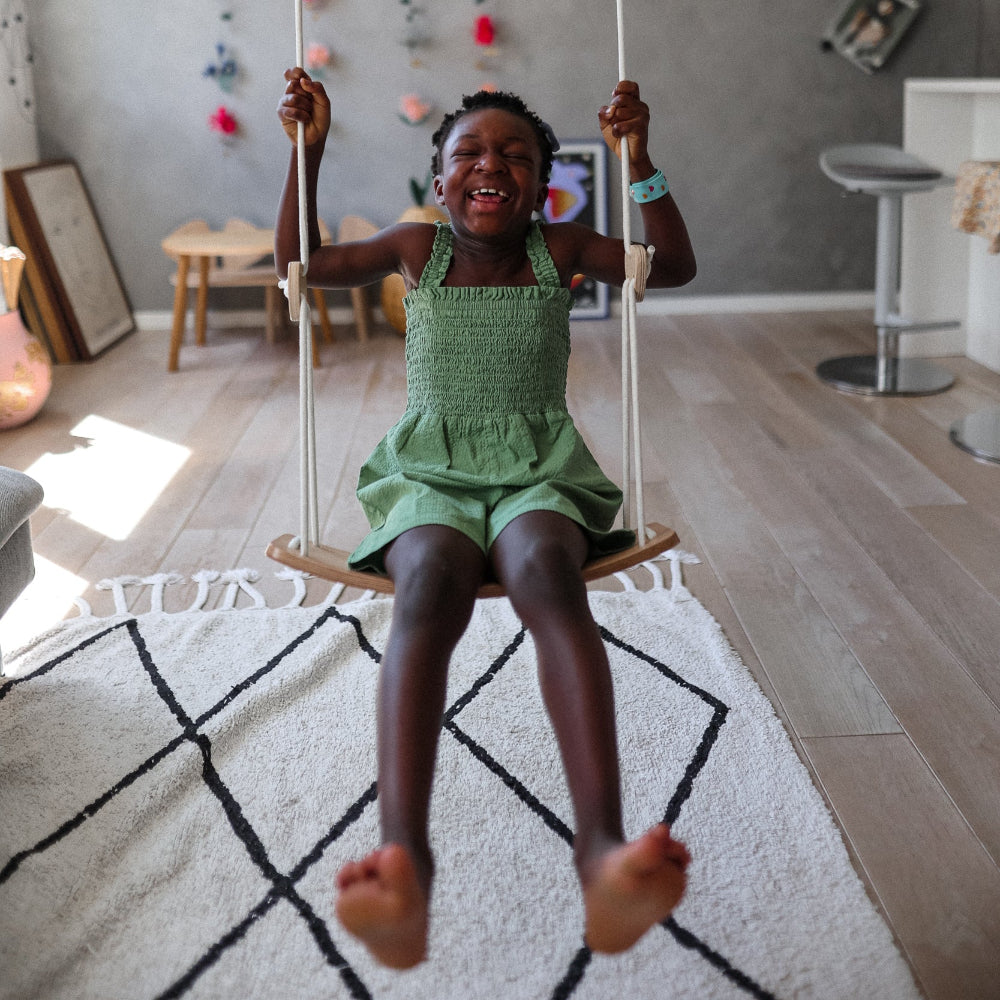 Child's wooden swing by Kinderfeets hanging from a sturdy frame, perfect for indoor or outdoor play and safe for kids.