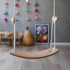 Kinderfeets child's swing hanging from a sturdy frame, featuring a wooden seat and safety straps for young children.