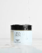 Oria Skin HydraDew Mask with hydrating ingredients, shown on a skincare display with fresh green leaves background.