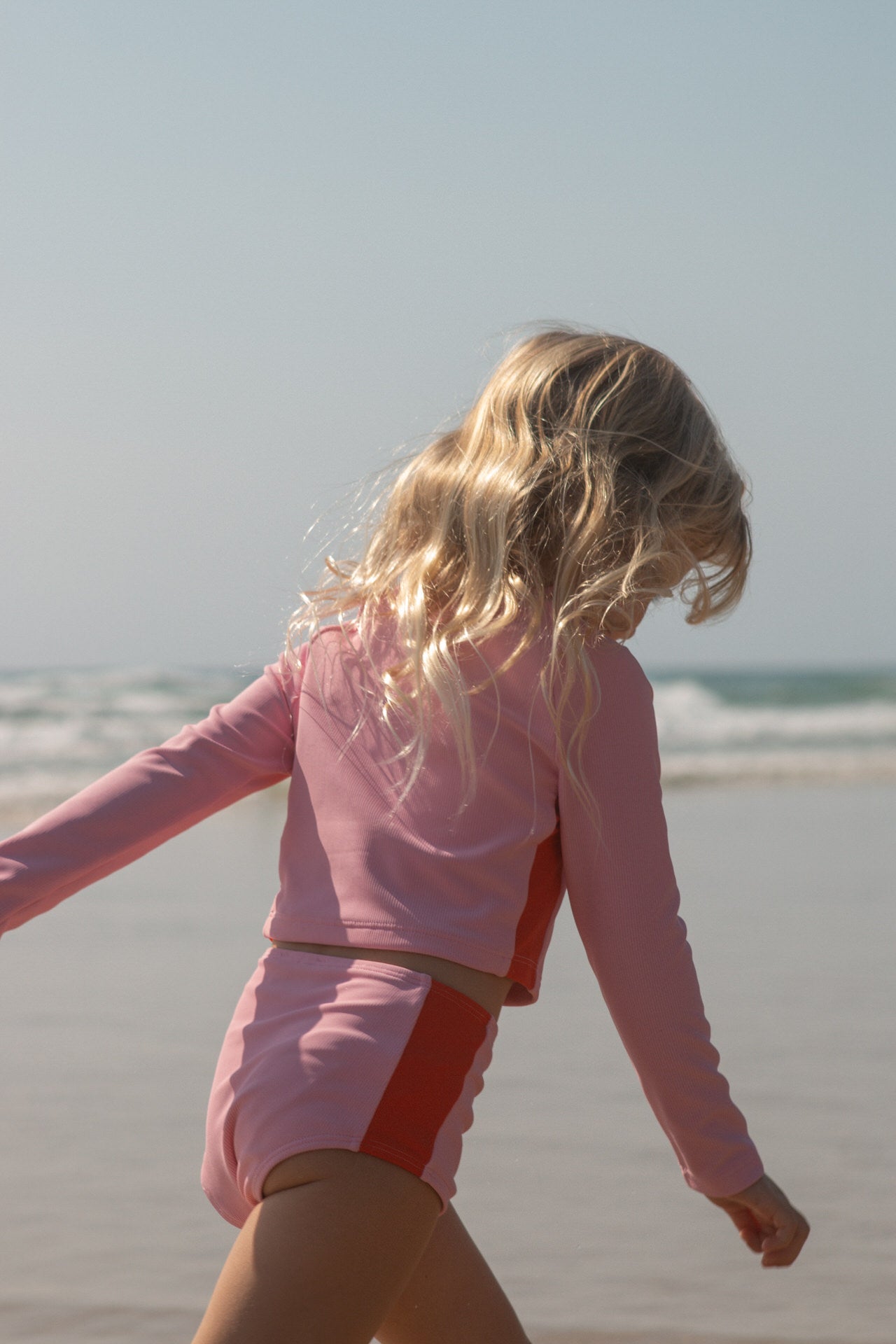 child in pink bikini walking on a beach with ocean view