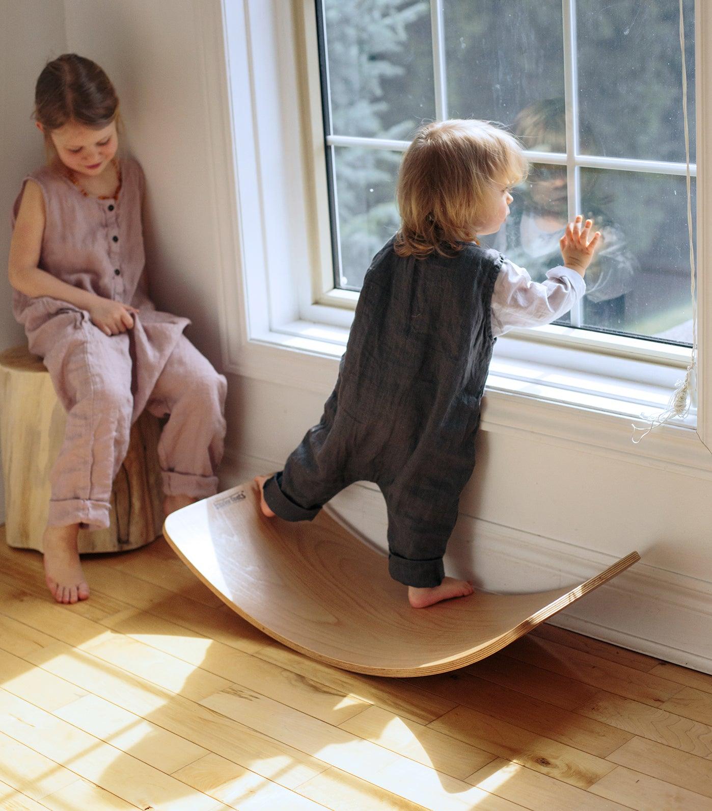 Kinderfeets Kinderboard in natural wood finish, shown in a lifestyle setting with children playing and balancing on the skate-inspired toy.