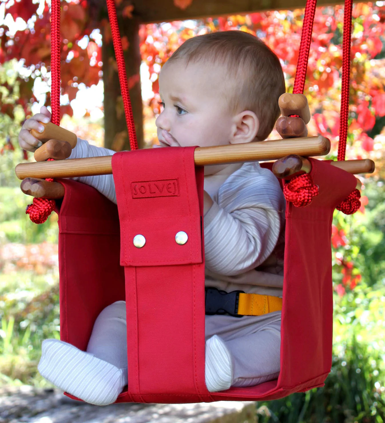 Red Pohutakawa toddler swing from Solvej Swings, outdoor toy with secure seat for babies and young children.