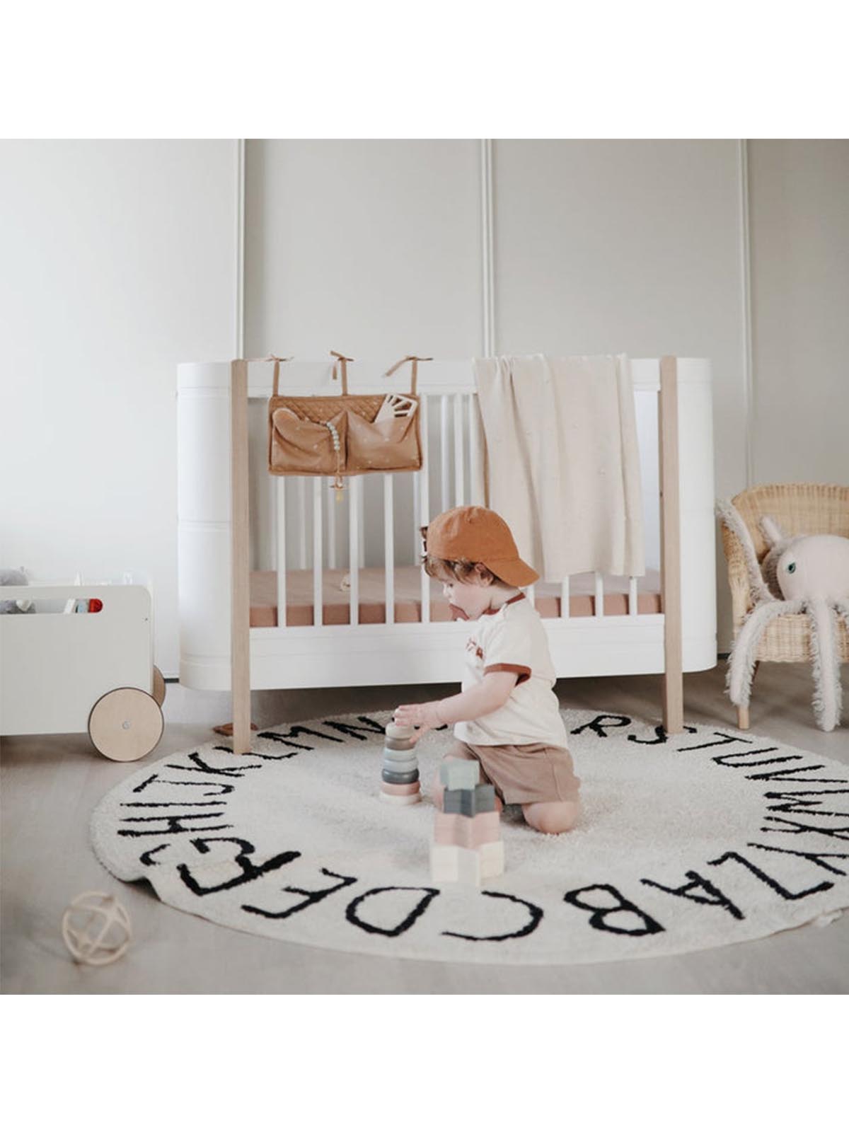 Mushie Crib Pocket with colorful rainbow design hanging on a crib side for easy storage and organization.