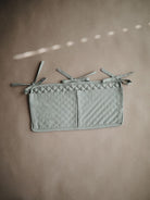 Mushie Roman Green crib pocket hanging on a crib, made of soft fabric, designed for storing small baby essentials.