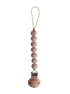 Mushie Cleo Pacifier Clip in blush attached to a matching pacifier holder with a soft blush-colored fabric and wooden clip.