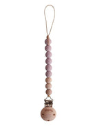 Mushie Cleo pacifier clip in mauve color attached to a pacifier case, showing soft fabric and clip details for baby accessories.